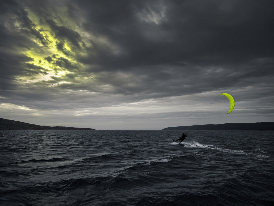 Kitesurf en un estrecho amplio, figura pequeña y cielo potente.